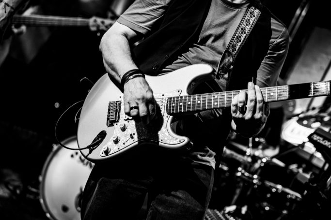 Man speelt elektrische gitaar op een podium in een band. Zwart-witfotografie.