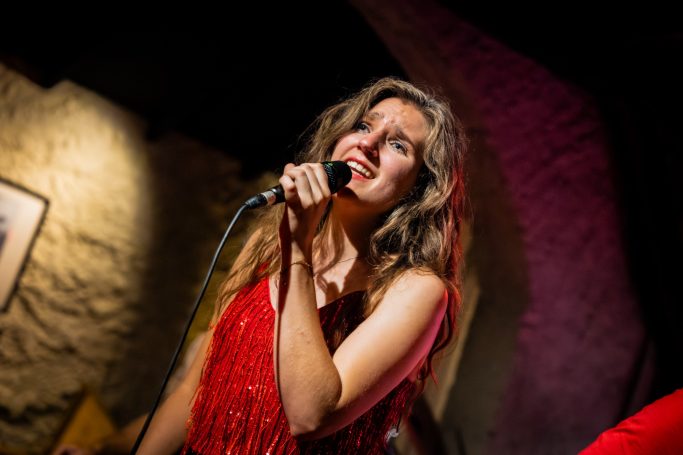 Zangeres in een rode outfit zingt met emotie op het podium.