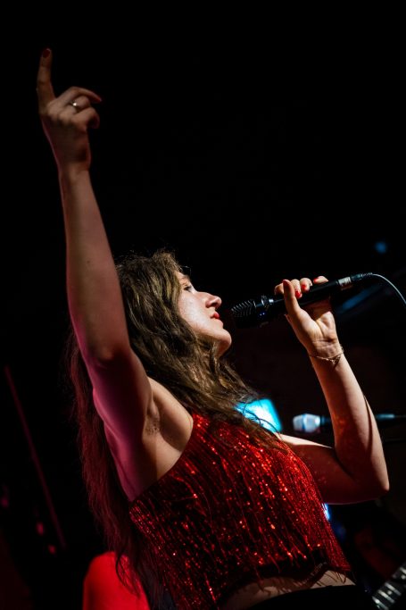 Zangeres met glinsterende top, zingt in microfoon met opgestoken arm.