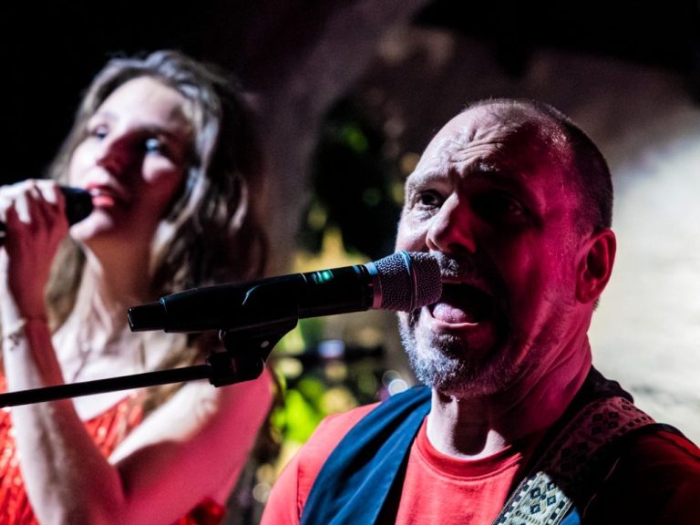 Zanger en zangeres performen samen op het podium met microfoons en levendige lichten.