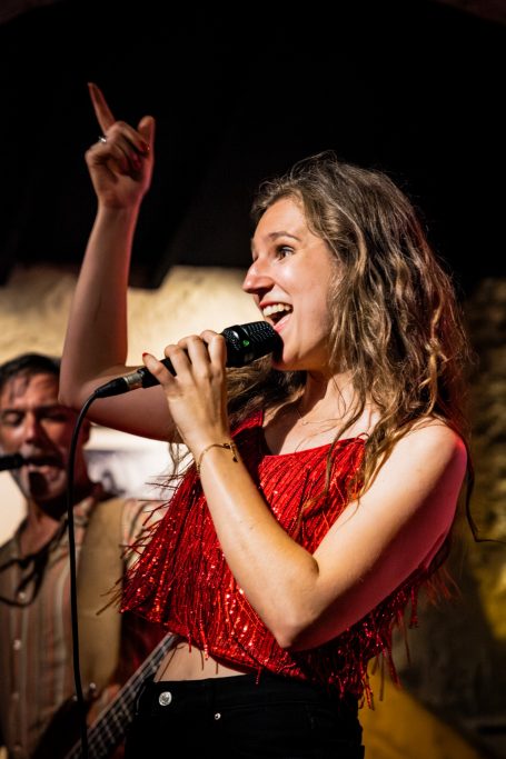 Zangeres met microfoon, wijzend en genietend van een live optreden.