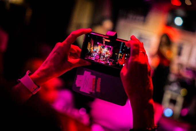 Een persoon neemt een foto van een optreden met een smartphone in een sfeervolle omgeving.