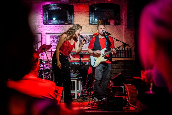 Zangeres en muzikant optreden op een levendig podium met kleurrijke verlichting.