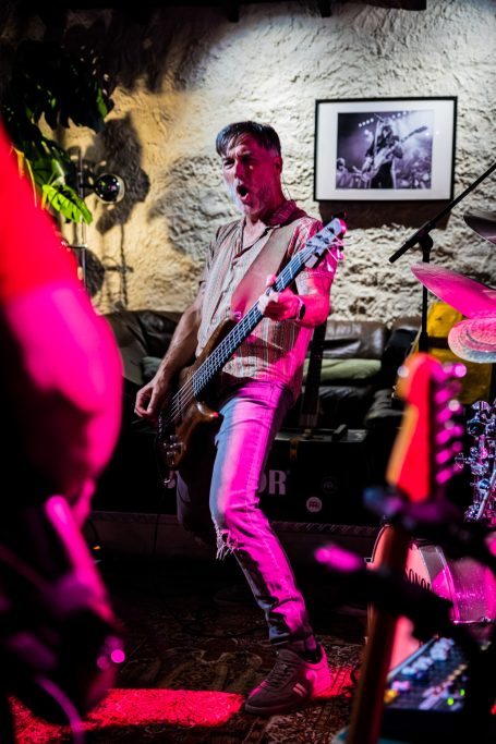 Een muzikant speelt basgitaar op een podium met kleurrijke verlichting.
