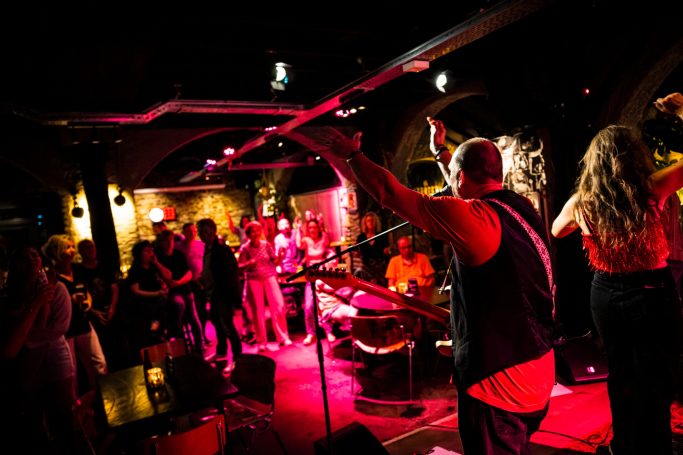 Een levendige muziekevenement met een band en dansend publiek in een sfeervolle setting.