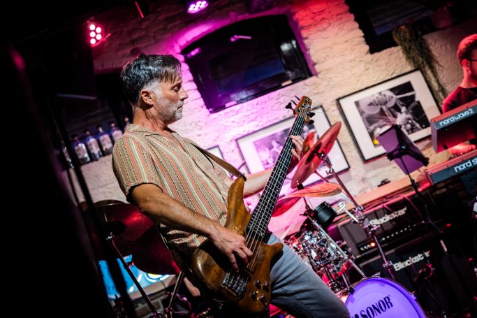 Muzikant speelt op een elektrische basgitaar op een podium met kleurrijke verlichting.