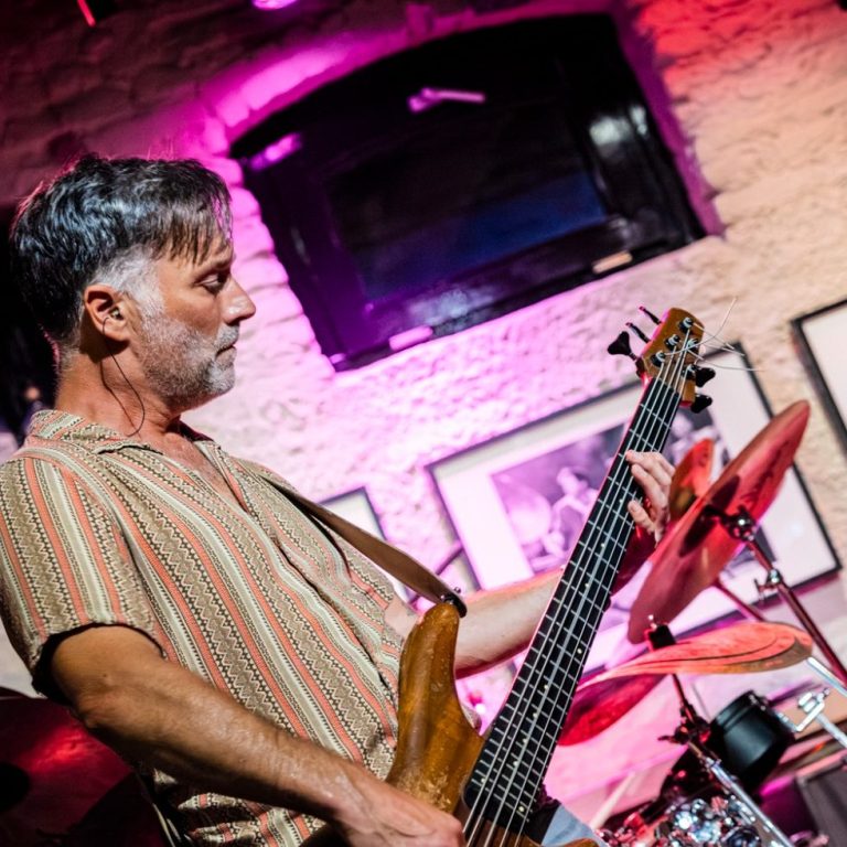 Muzikant speelt basgitaar op een podium met kleurrijke verlichting.