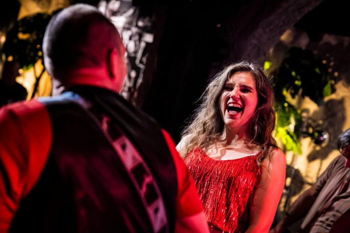 Woman in a red dress singing passionately to a male performer on stage.