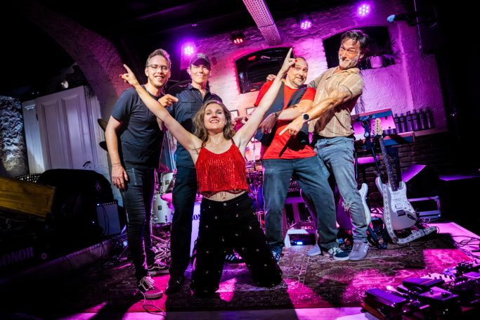 Vijf muzikanten poseren op het podium met kleurrijke verlichting.