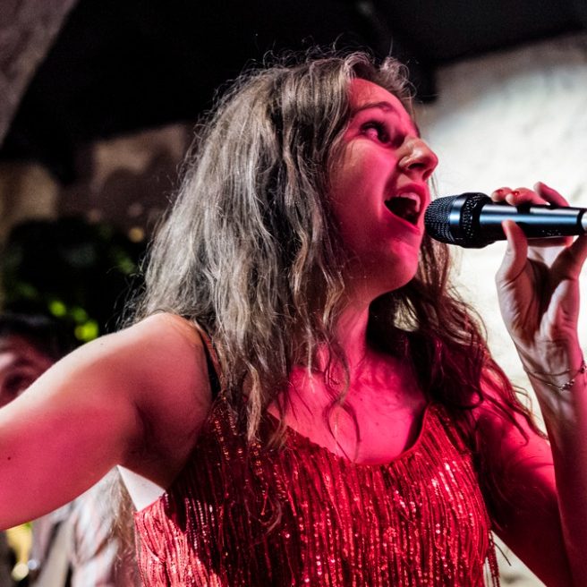 Zangeres met microphone in hand, gekleed in een glinsterend top, zingt vol passie.